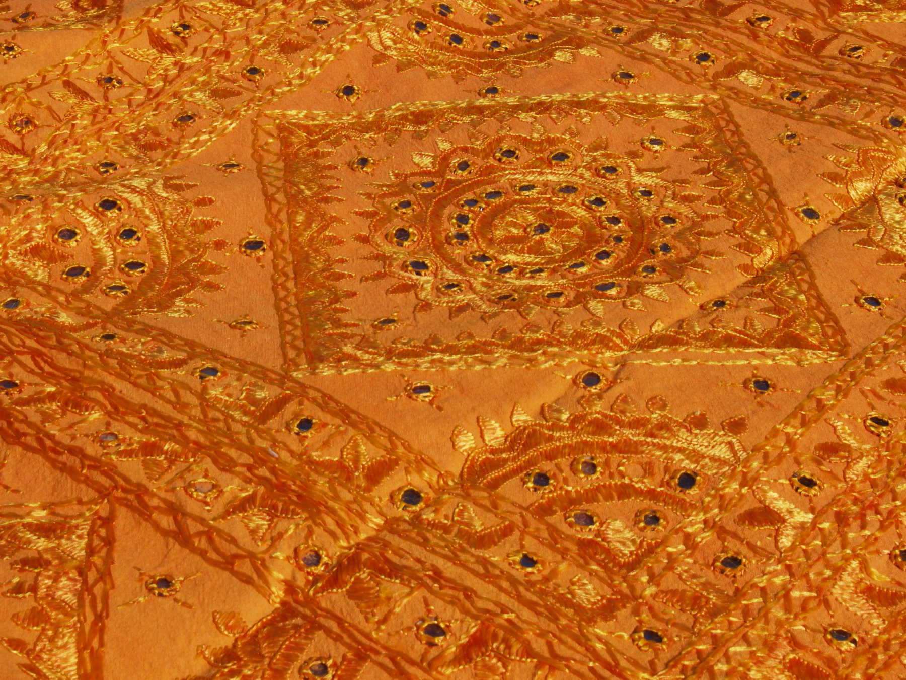 Telo Indiano in cotone doppio strato, ricamato tono su tono con specchietti,  di color arancione. Può essere impiegato come copridivano, copriletto, tovaglia o tessuto da appendere a parete. Dimensioni 215x270cm