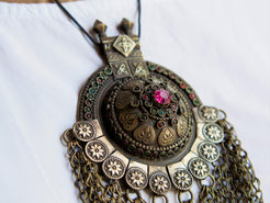 Questa lunga e massiccia collana proviene probabilmente da una delle tribù nomadi dell'Afghanistan o del Turkmenistan. Il ciondolo ha inscritto motivi floreali e boteh (paisley). Costruito in lega di argento, pezzo unico databile primi 900, conservato perfettamente, le catene che all'estremità hanno una sfera campanellino sono originali e incastrate a mano. Pezzo di difficile reperibilità.  lunghezza totale 20 cm, diametro parte superiore 10 cm, peso 170 gr