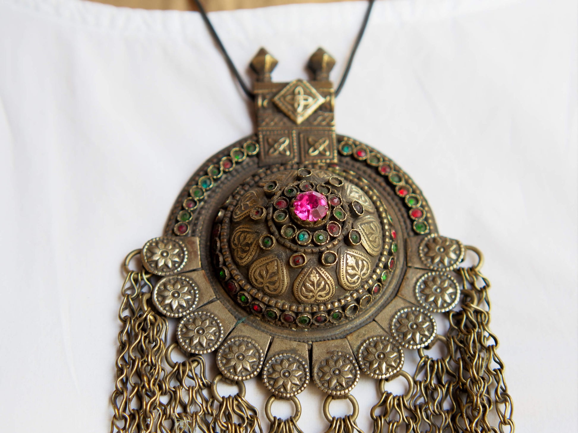 Questa lunga e massiccia collana proviene probabilmente da una delle tribù nomadi dell'Afghanistan o del Turkmenistan. Il ciondolo ha inscritto motivi floreali e boteh (paisley). Costruito in lega di argento, pezzo unico databile primi 900, conservato perfettamente, le catene che all'estremità hanno una sfera campanellino sono originali e incastrate a mano. Pezzo di difficile reperibilità.  lunghezza totale 20 cm, diametro parte superiore 10 cm, peso 170 gr