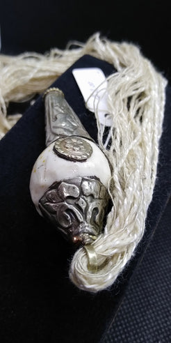 pendaglio raffigurante una conchiglia tibetana con argento cesellato e corallo . oggetto di culto di cultura buddista , strumento rituale. Era già utilizzata in epoca prebuddhista come simbolo delle divinità femminili, come contenitore e come strumento musicale rituale. Nel Buddhismo tibetano si utilizza spesso come strumento musicale e il suo potente suono viene utilizzato per richiamare i monaci alle riunioni, per fare offerte di suono durante le puje. Rappresenta la gloria dell’insegnamento del Dharma, c